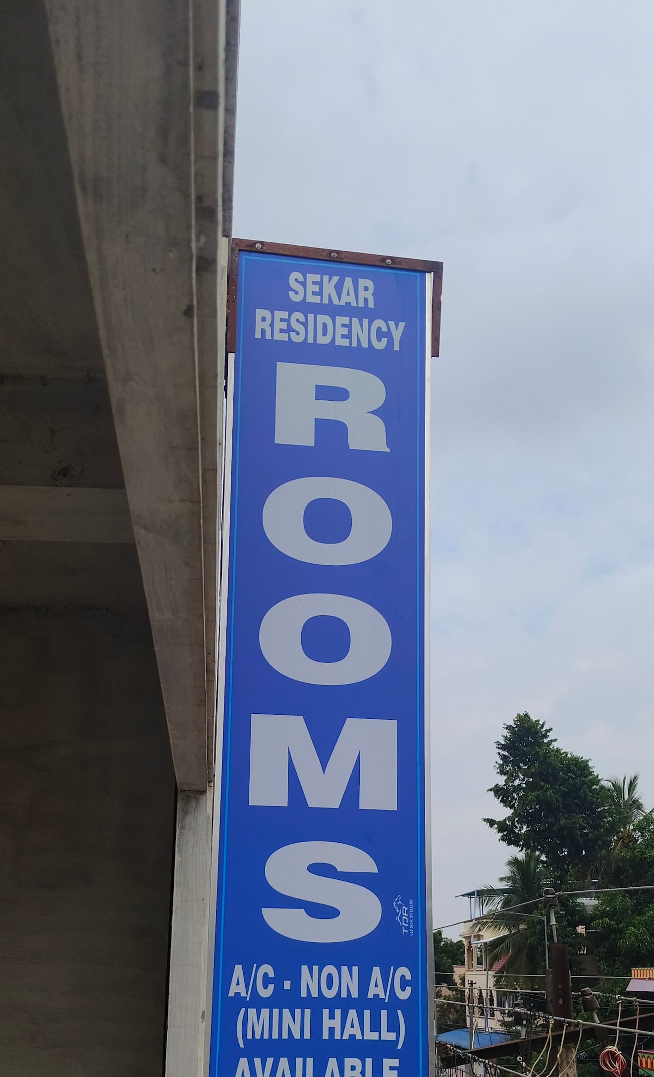 Vertical blue sign for Sekar Residency advertising rooms, A/C, and a mini hall available.