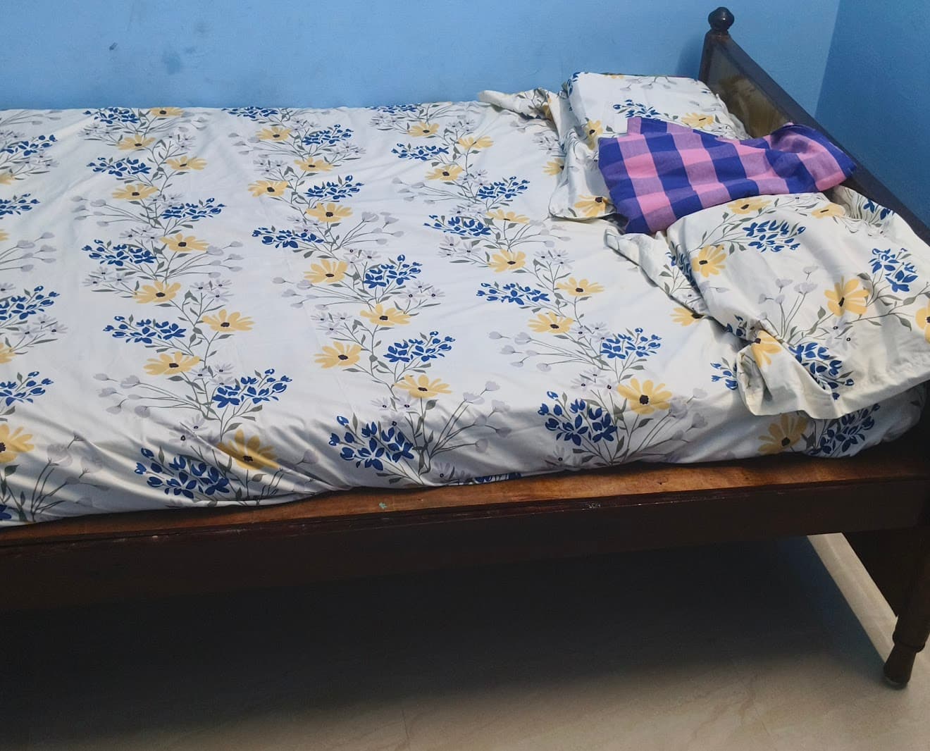 Wooden bed with blue and yellow floral bedding and a purple checkered cloth on top.